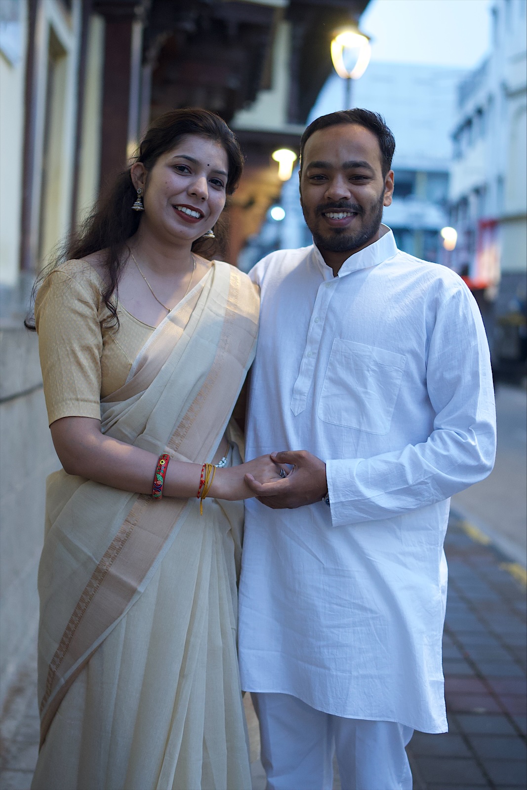 Suyash and Astha smiling, hand in hand, on an evening street
